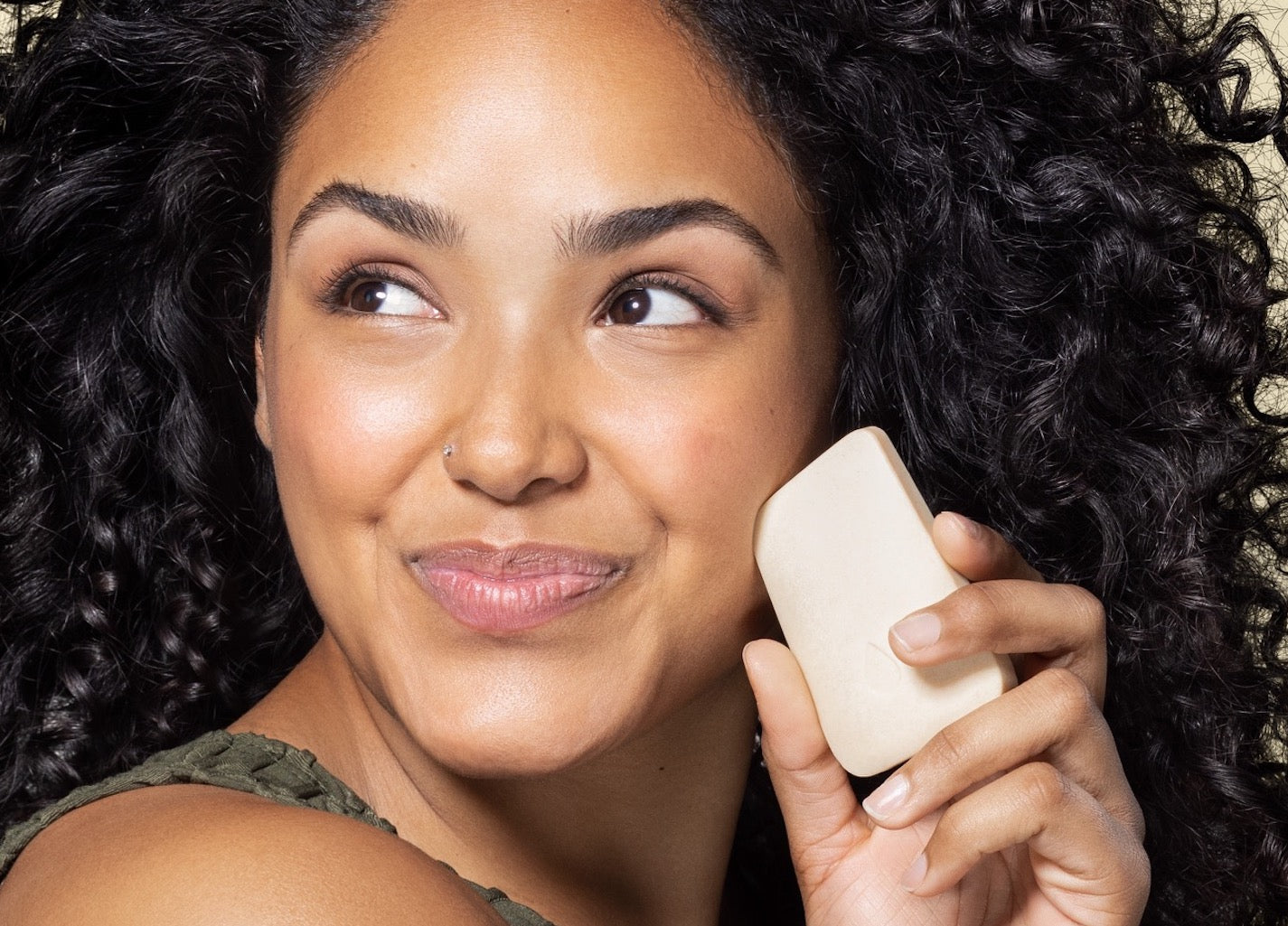 Woman holding face wash bar near skin to show size of bar