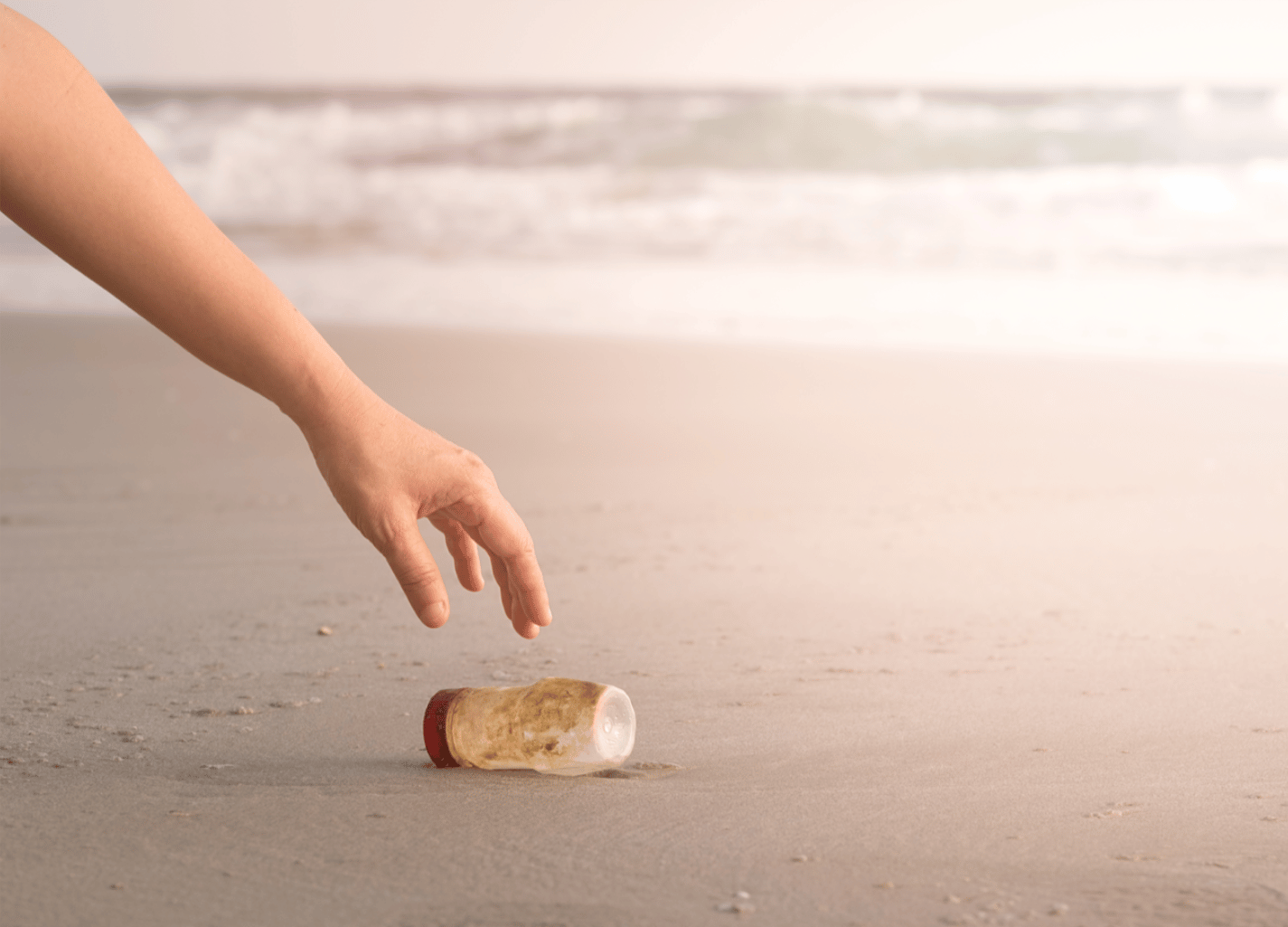 person picking up a plastic bottle of the beach