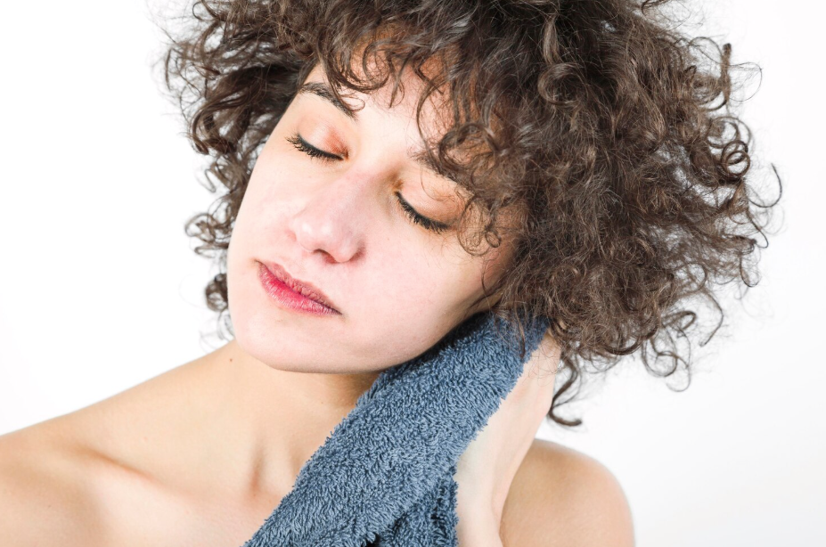 A curly haired woman drying her hair with a blue towel.