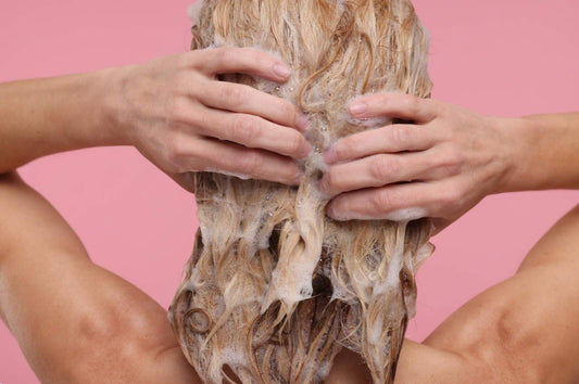 Blonde haired woman washing wavy hair on a pink background.