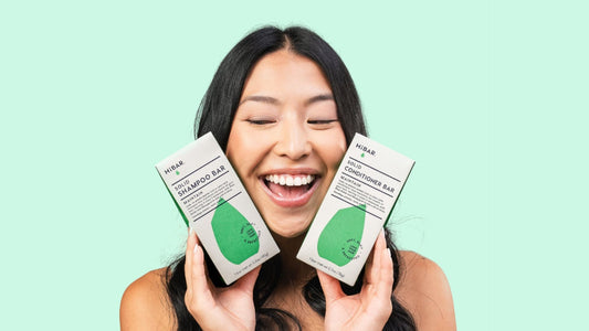A female model holding two haircare bars against a light green background.