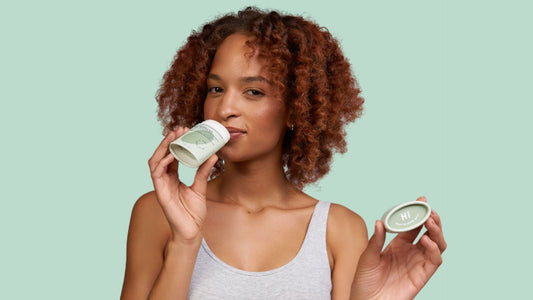 Woman with dark curly hair holding a green deodorant bar on a light green background.