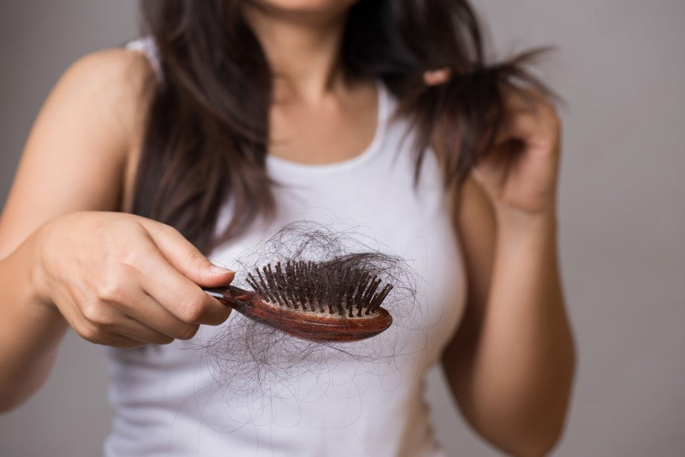 Woman holding hair brush with clumps of dark hair.