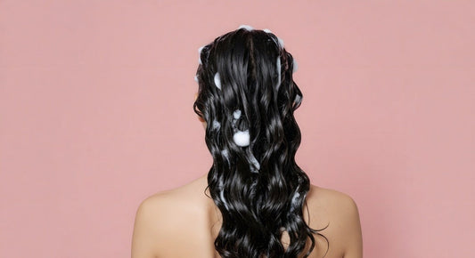 Woman with suds on wavy black hair on a pink background.