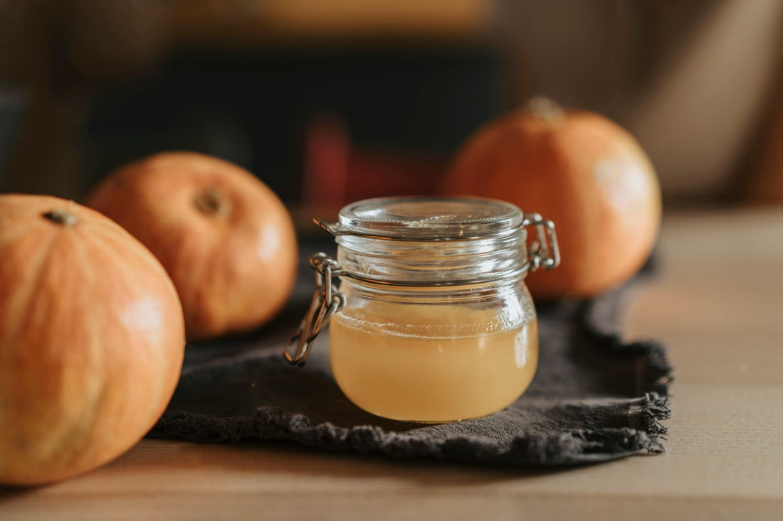 A small jar of apple cider vinegar surrounded by apples.