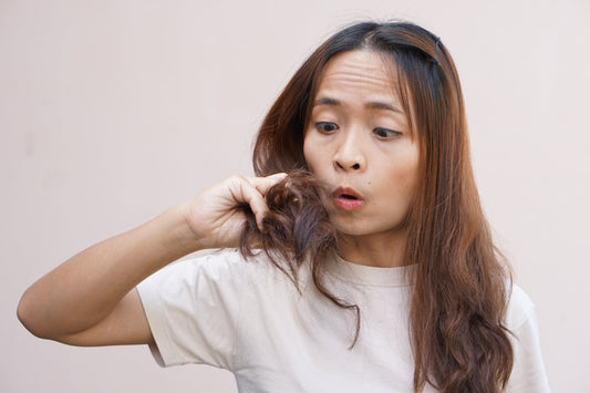 Brown haired woman holding hair split ends on a light background.