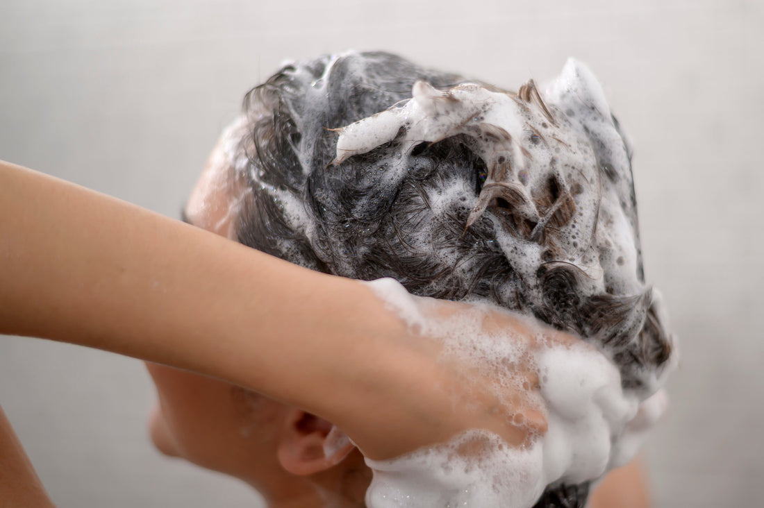 Black haired woman washing dark wavy hair on a white background.
