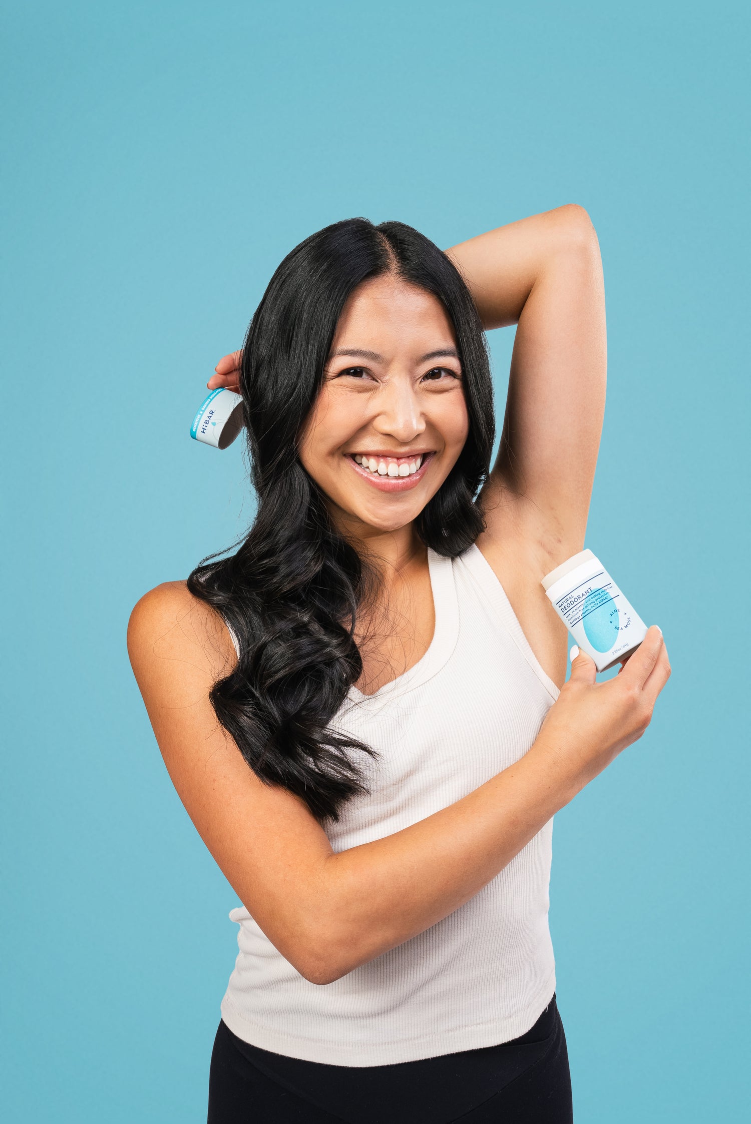 Model with dark hair using a blue deodorant bar on a blue background.