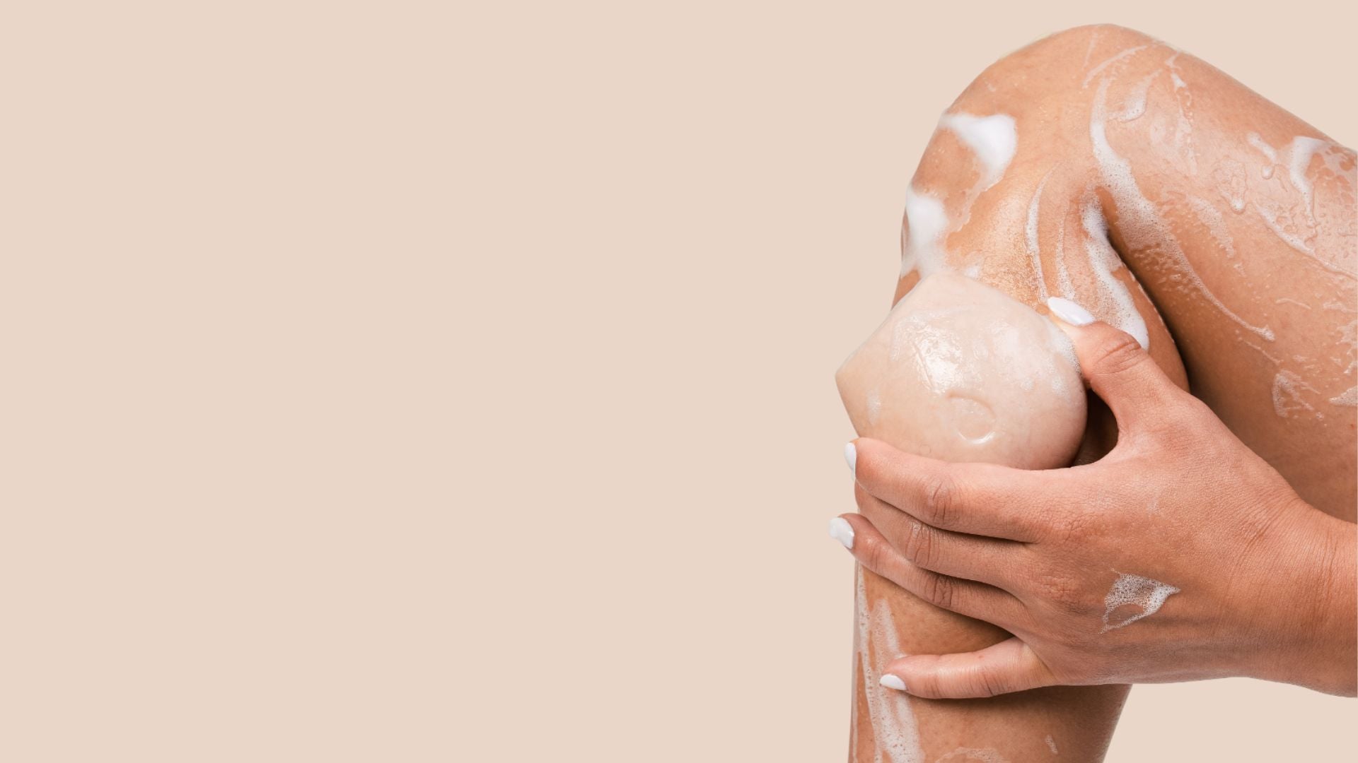 Woman holding up a beige body wash bar on her leg against a light brown background.