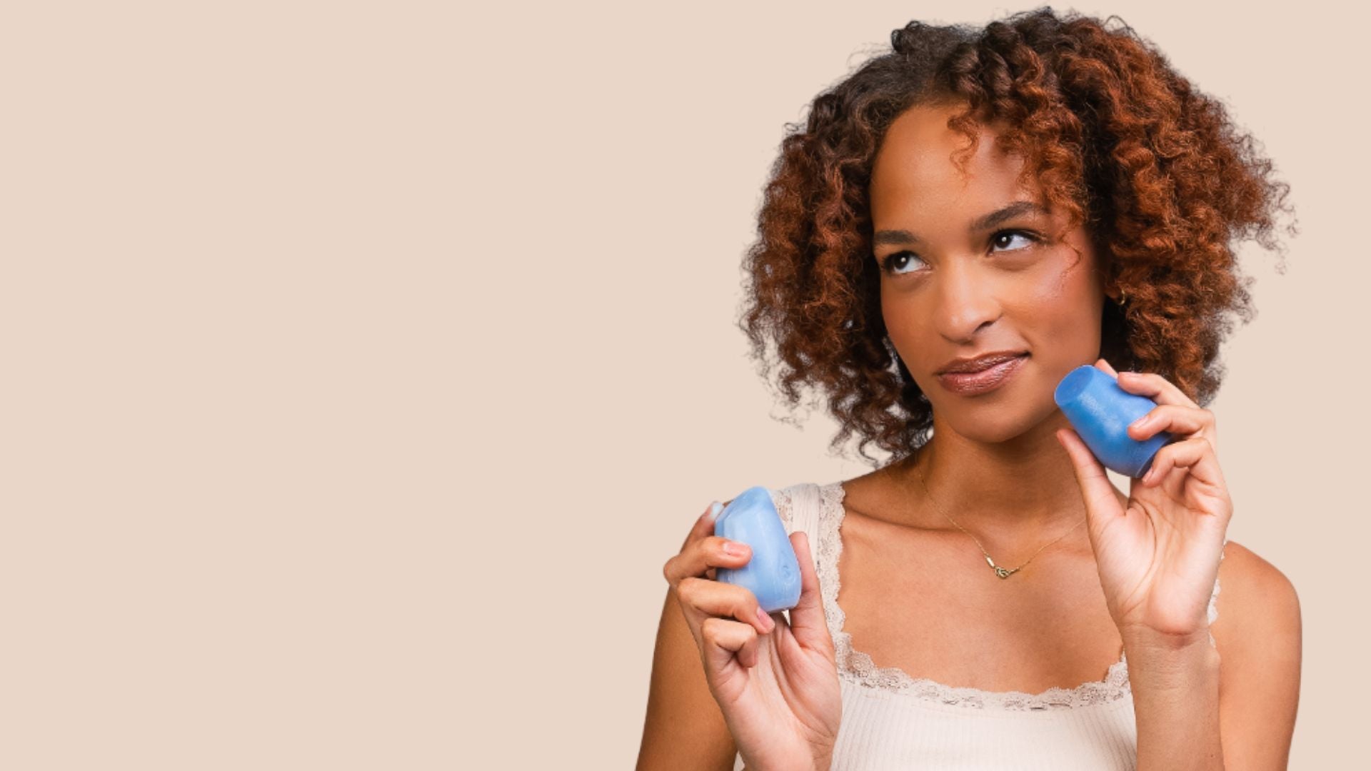 Woman with curly dark hair holding two haircare bars on a beige background.