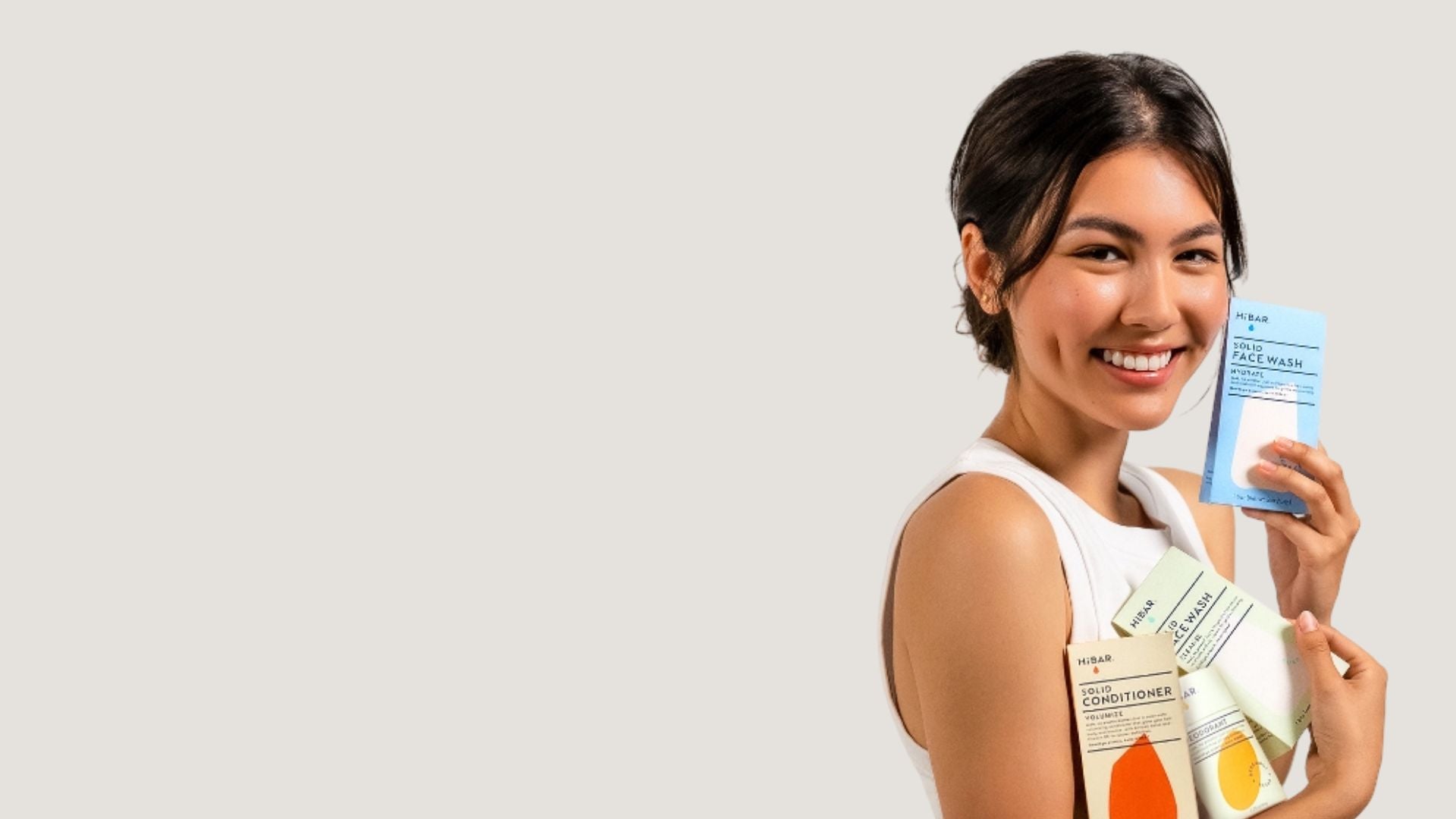 Model with dark hair holding various HiBAR products on a white background. 