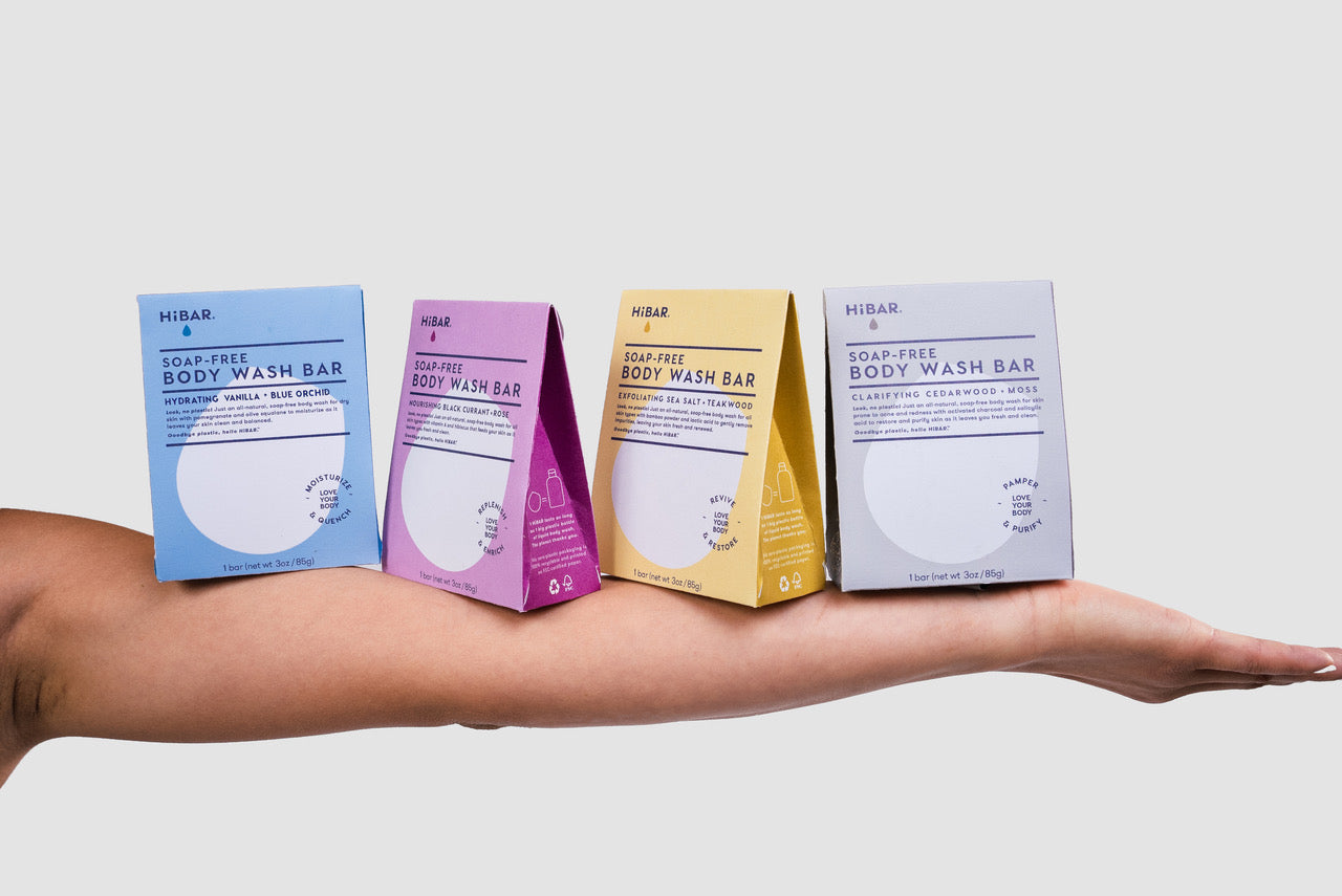 Person holding four body wash bar packages on their arm on a white background. 