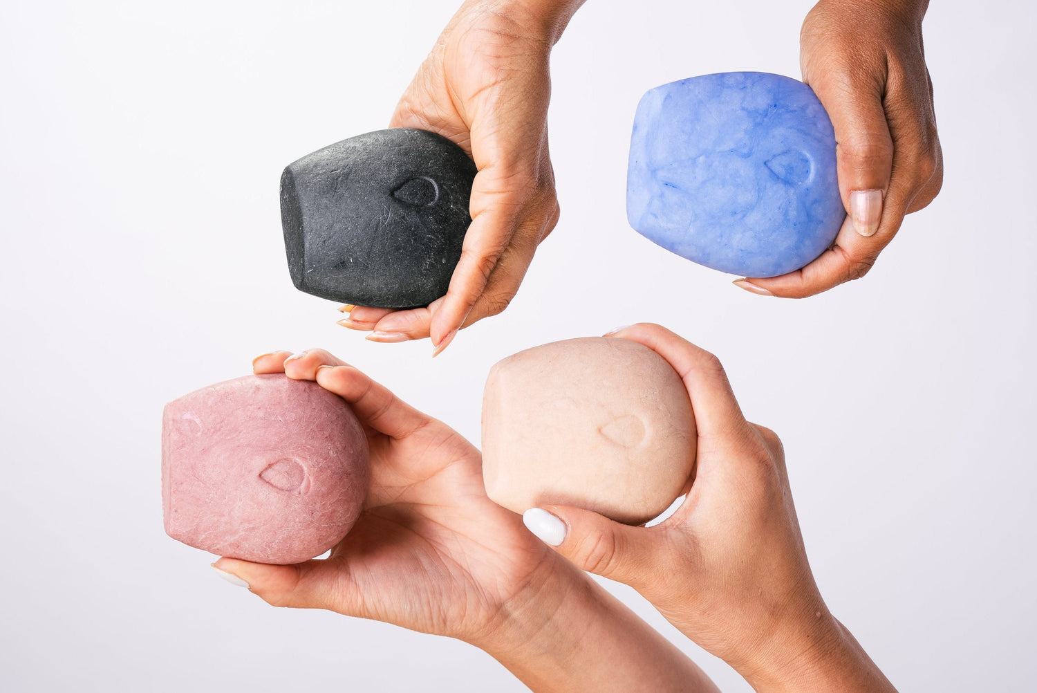 Four hands holding four body wash bars on a white background.