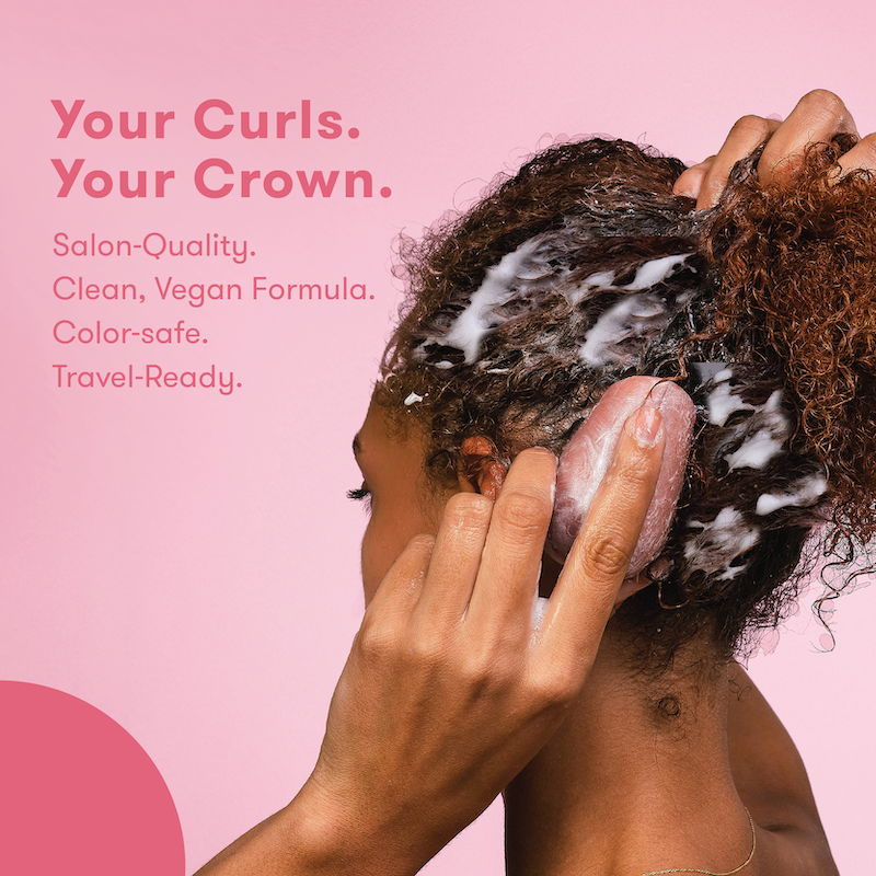 Picture of a woman with lathered hair, holding HiBAR shampoo bar against her head with text that reads: Your Curls. Your Crown. Salon Quality. Clean, Vegan Formula. Color-safe. Travel-Ready.