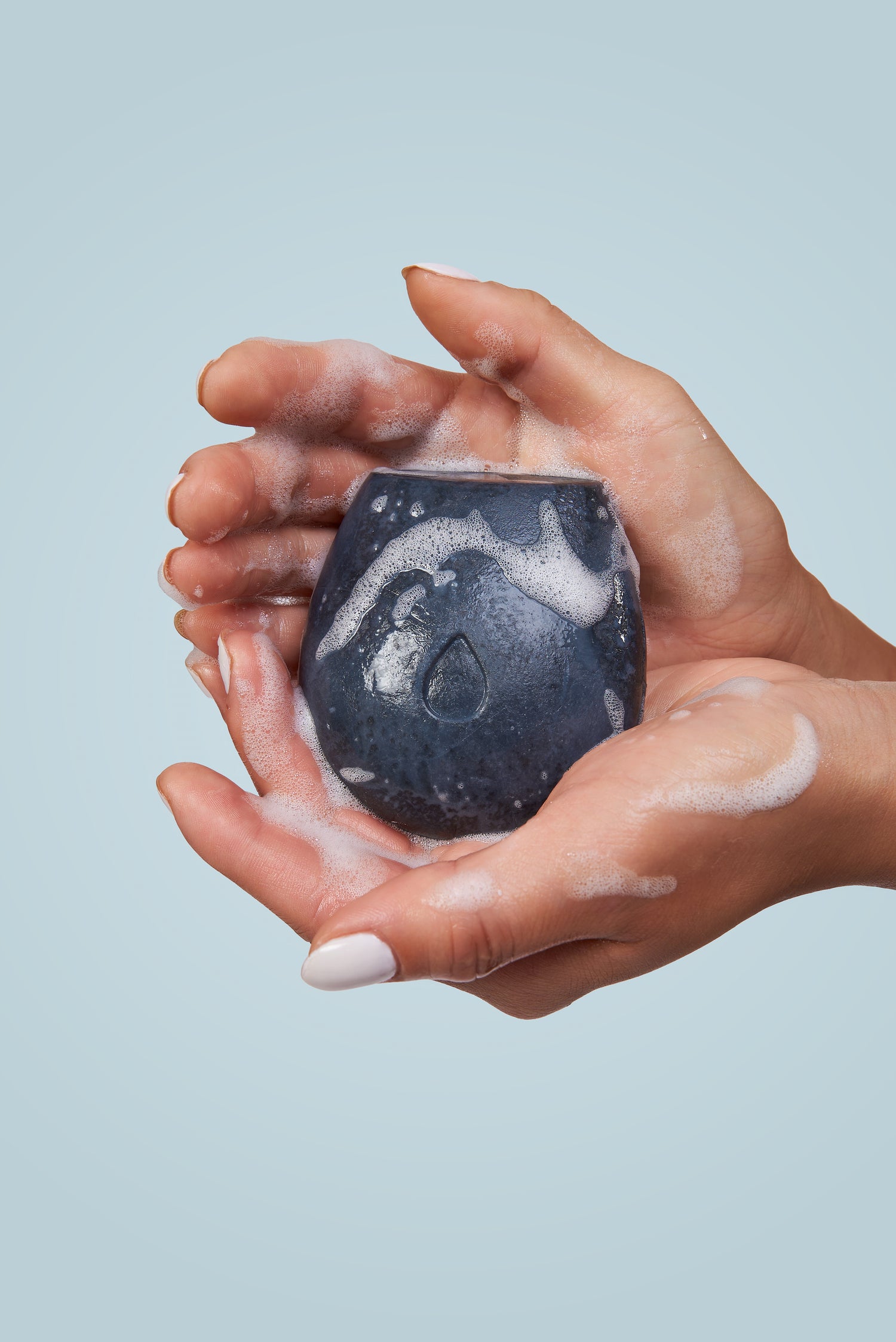 Model holding a lathering black body wash bar on a blue background.