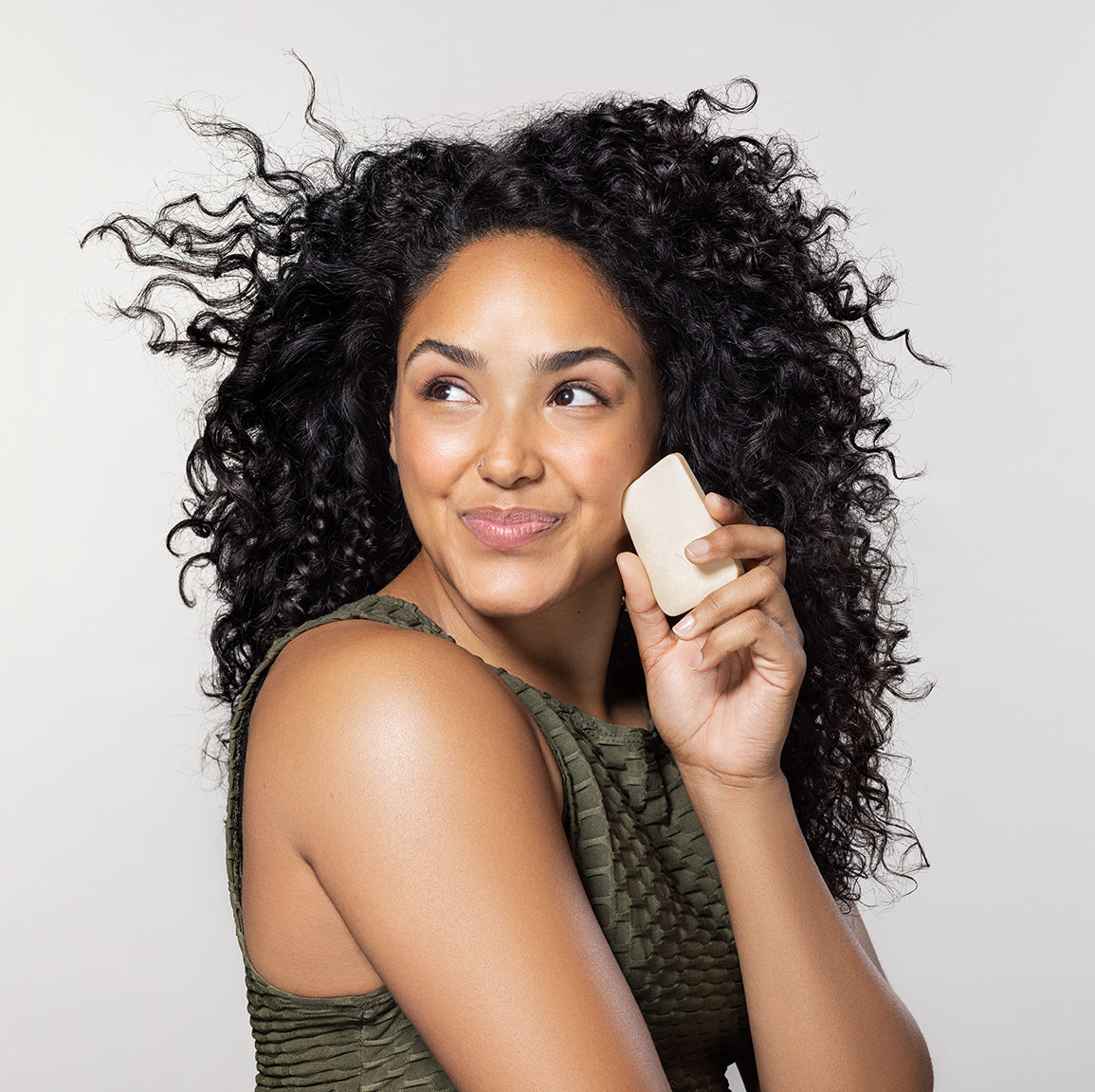Model with curly hair holding a face wash bar on a white background.
