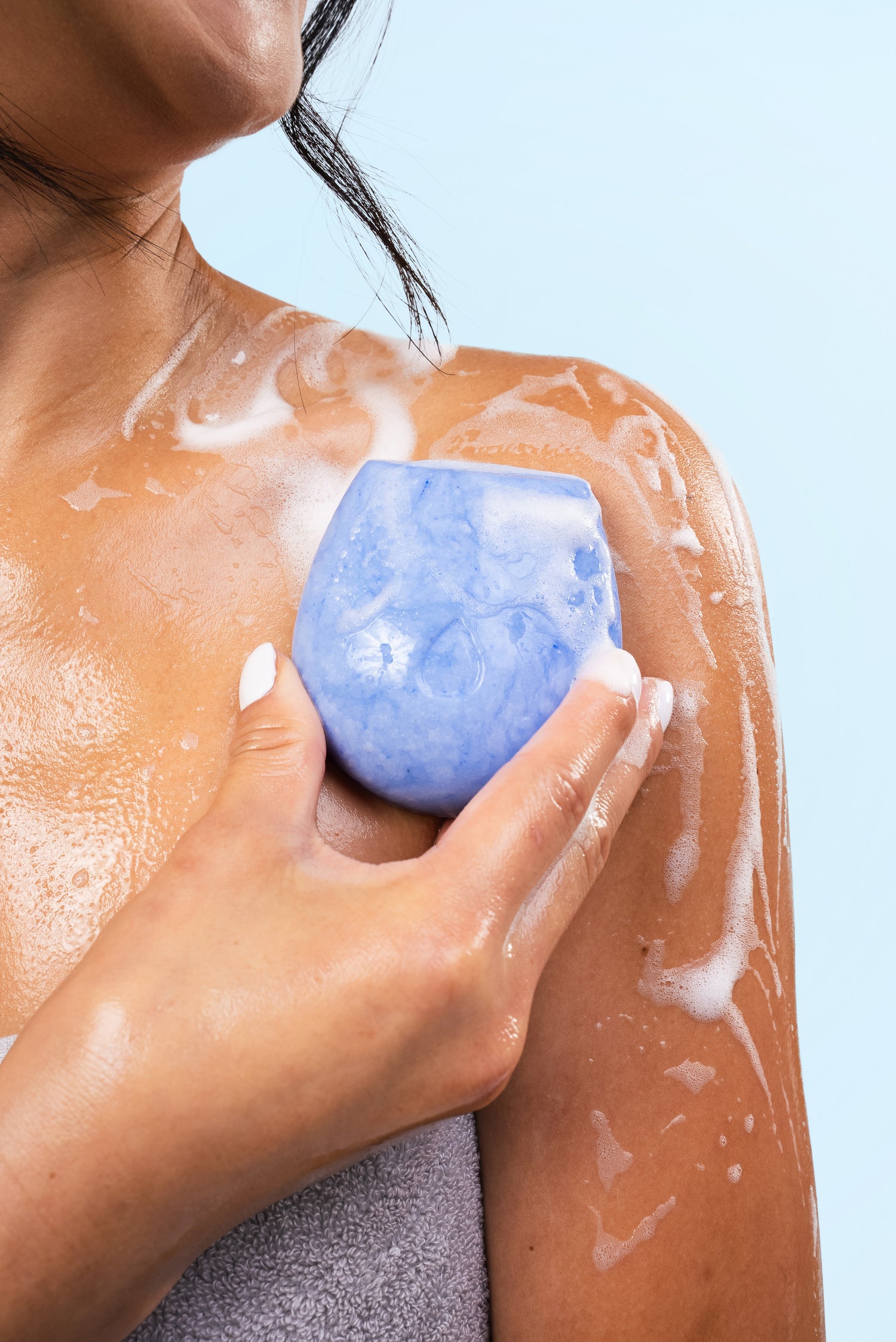 Model holding a blue body wash bar on her shoulder against a blue background.