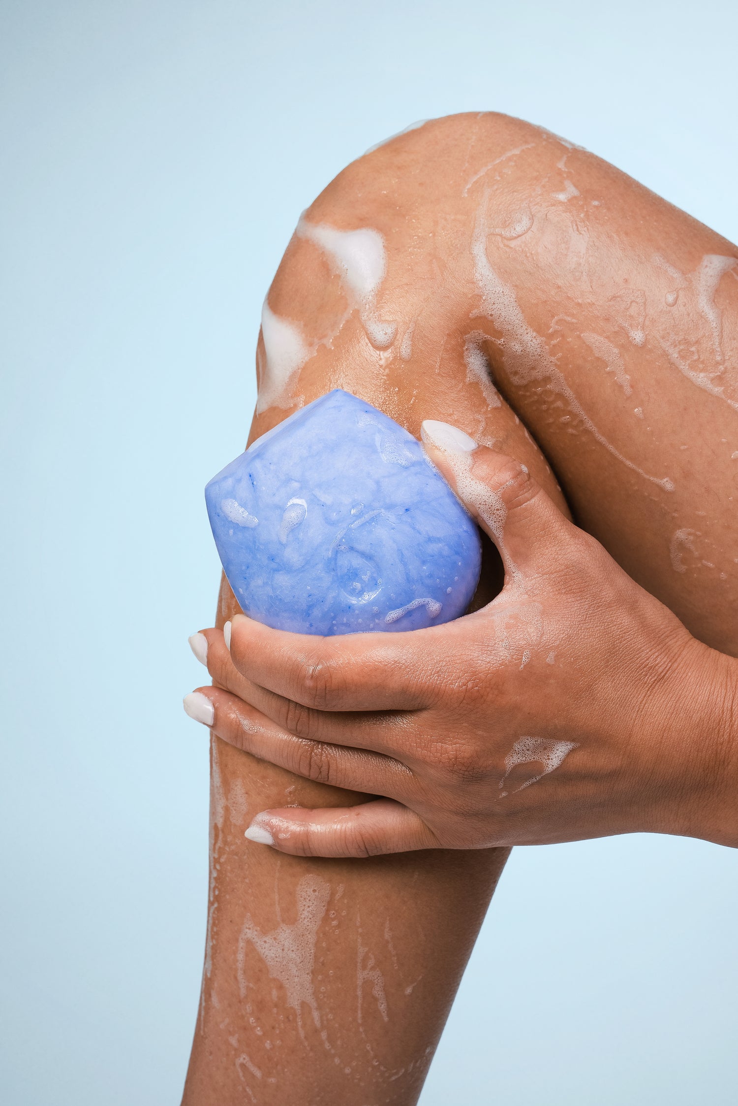 Model washing their leg with a blue body wash bar on a blue background.