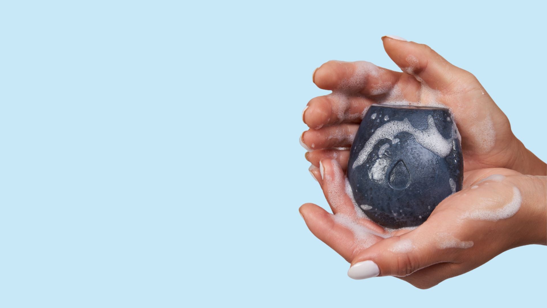 A woman's hand holding a black body wash bar on a blue background.