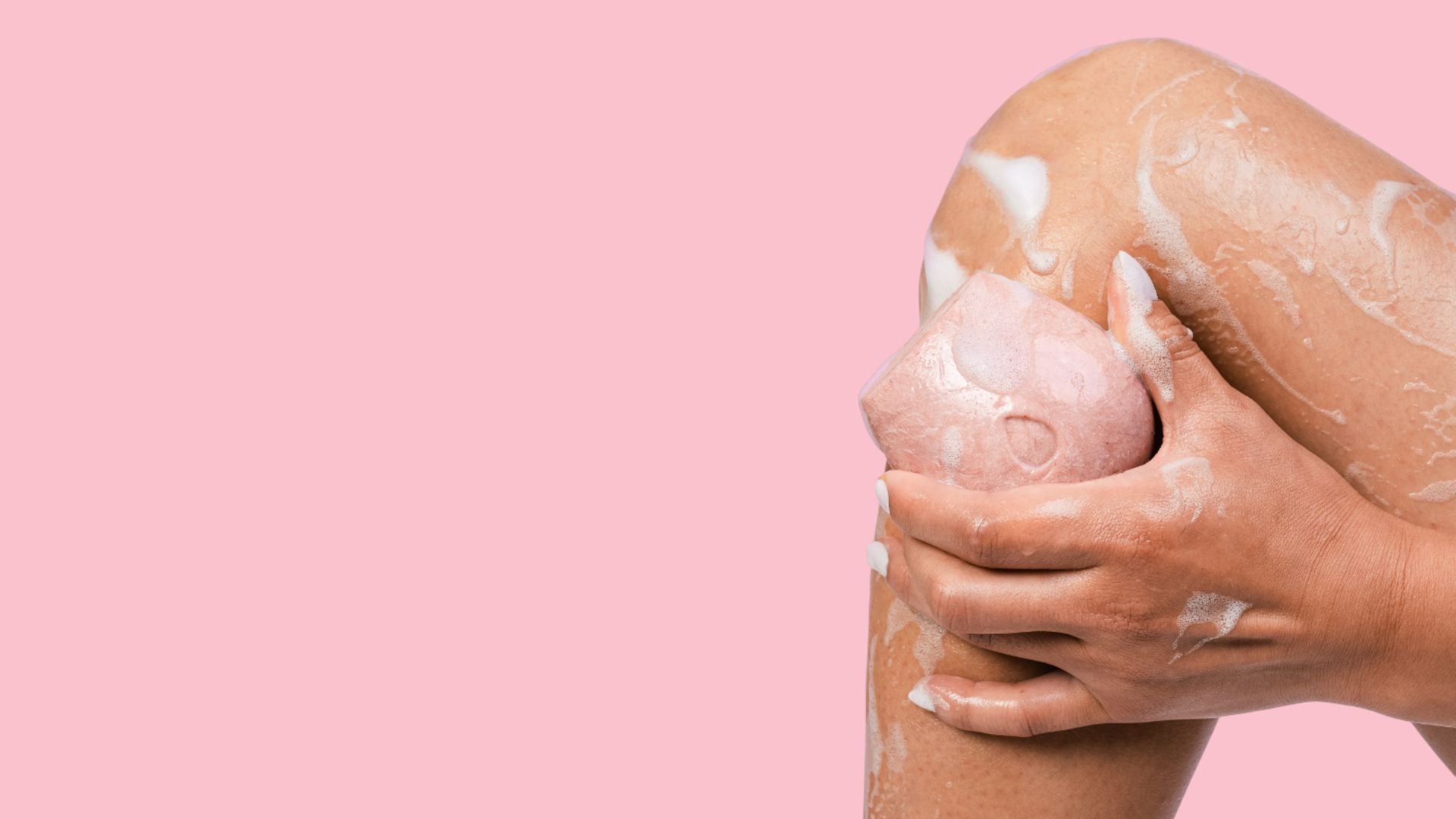 Female model washing her leg with a pink body wash bar on a pink background.
