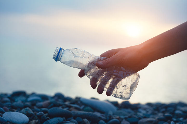 person holding a plastic bottle above the shore during a sunset