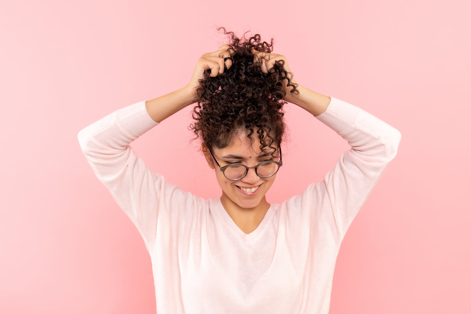 Curly haired model holding her hair against a pink background.