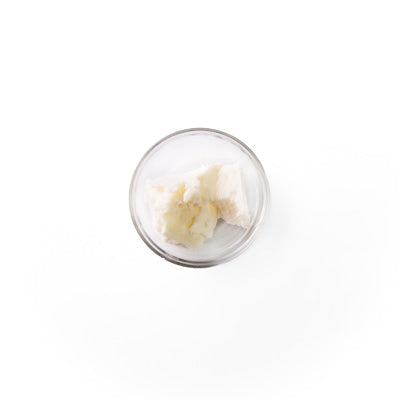 shea butter in a glass dish. It is an white colored butter-like solid.