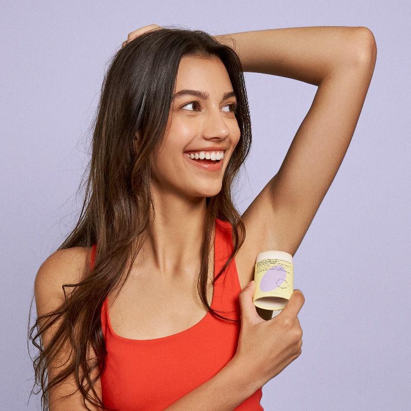 Woman applying lavender and jasmine deodorant under her arm.